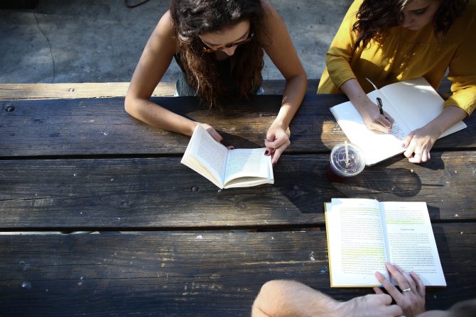 three people reading on a wooden table