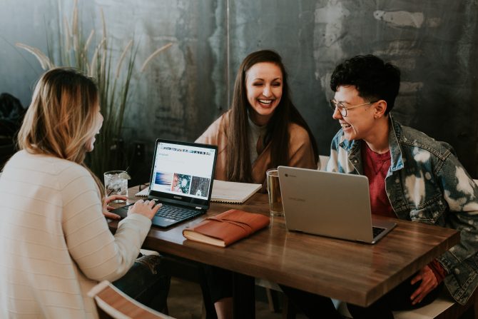 three people laughing with open laptops