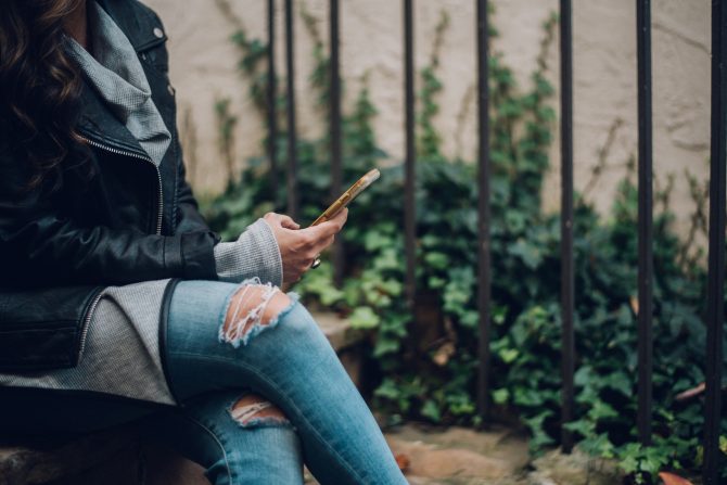 crossed legs with ripped jeans, holding a phone