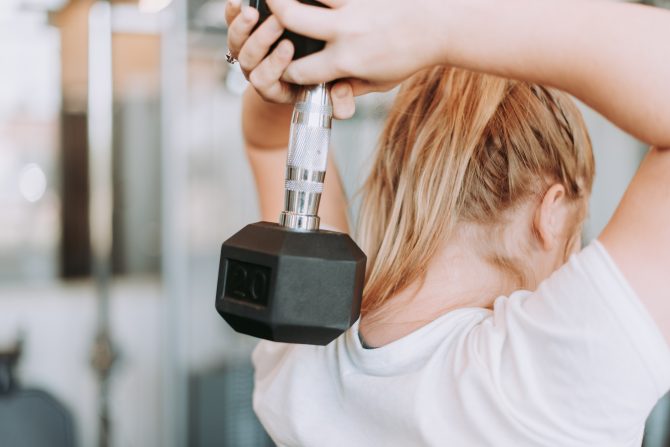 woman holding dumbbell behind neck