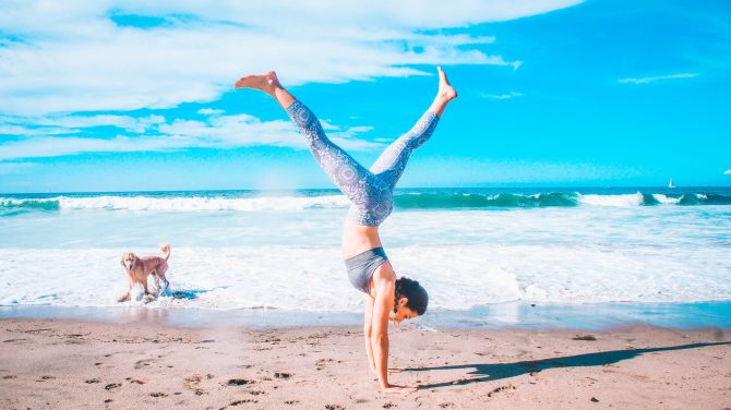 woman performing inverted stand beside seashore