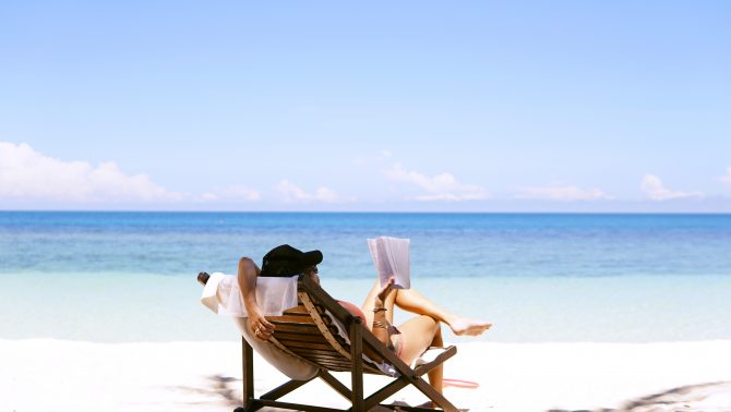 woman sitting on a beach reading, avoid the summer scaries